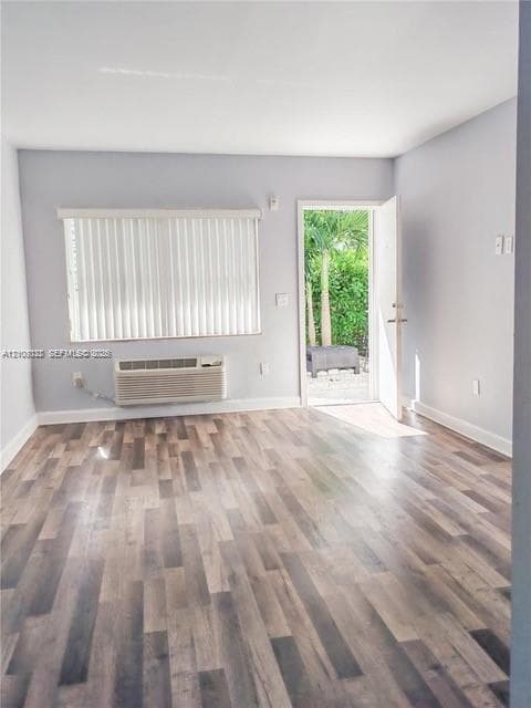 Room featuring wood-finish flooring, a wall-mounted climate control unit, a window with horizontal blinds, and an exterior door