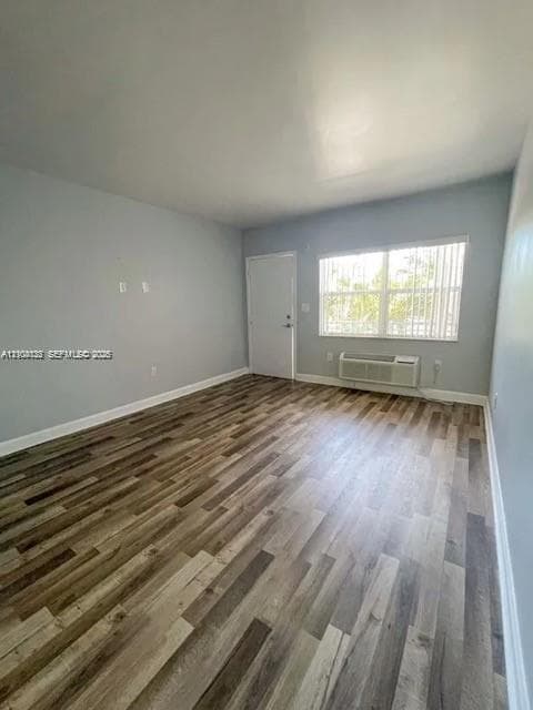 Wood-finish flooring, neutral wall tones, multi-pane window with vertical blinds, and wall-mounted air conditioning unit