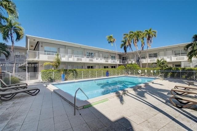 Outdoor swimming pool featuring a concrete deck, white metal perimeter fencing, and mature palm trees