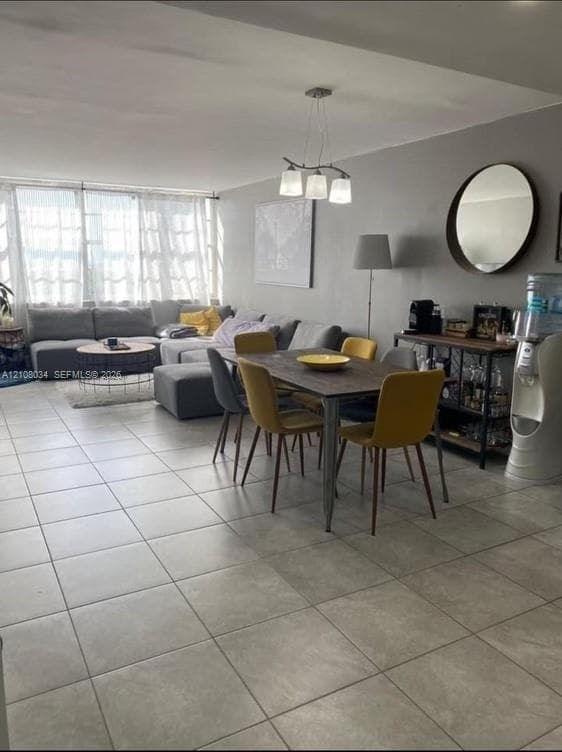 Open-concept room featuring large-format ceramic tile flooring, neutral wall tones, multi-light brushed-metal chandelier, and expansive windows