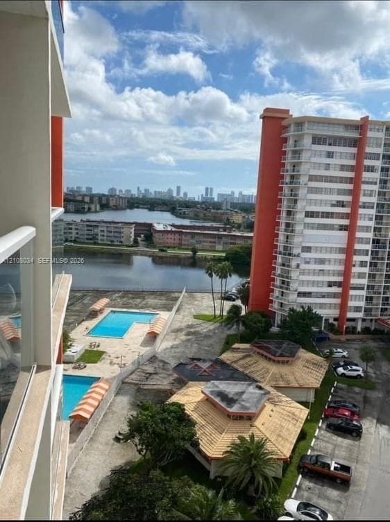 Elevated terrace featuring a glass panel railing, two outdoor swimming pools, and scenic water and urban skyline backdrop