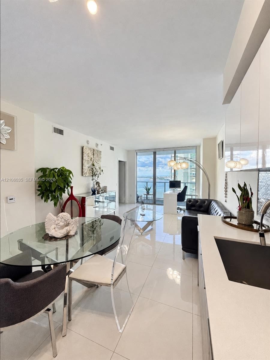 Open-concept living space featuring high-gloss cabinetry, stone countertops, large-format tile flooring, and floor-to-ceiling glass doors opening to a balcony