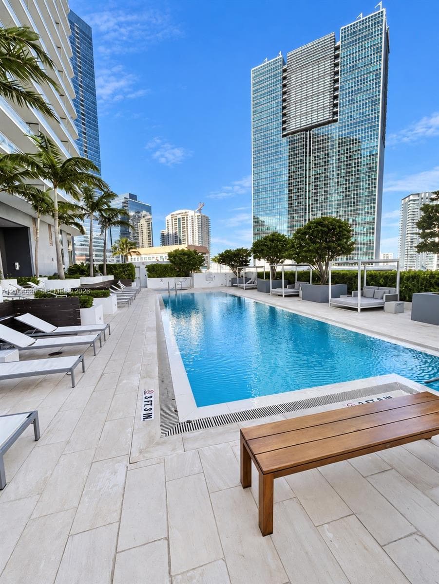 Swimming pool featuring light-toned stone decking, mature landscaping, and built-in privacy hedges
