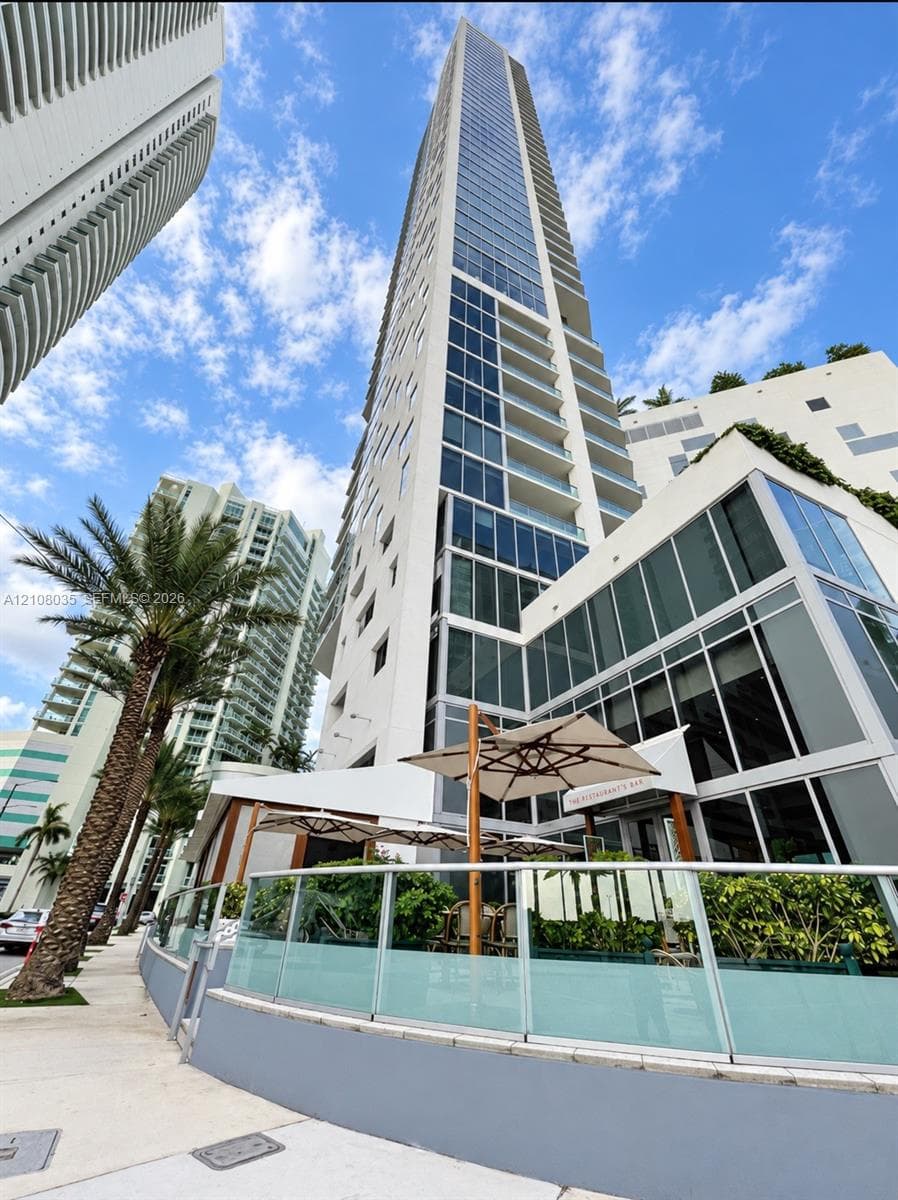 High-rise residential tower featuring a glass and concrete facade, wrap-around balcony levels, and an expansive ground-level terrace with integrated glass railings