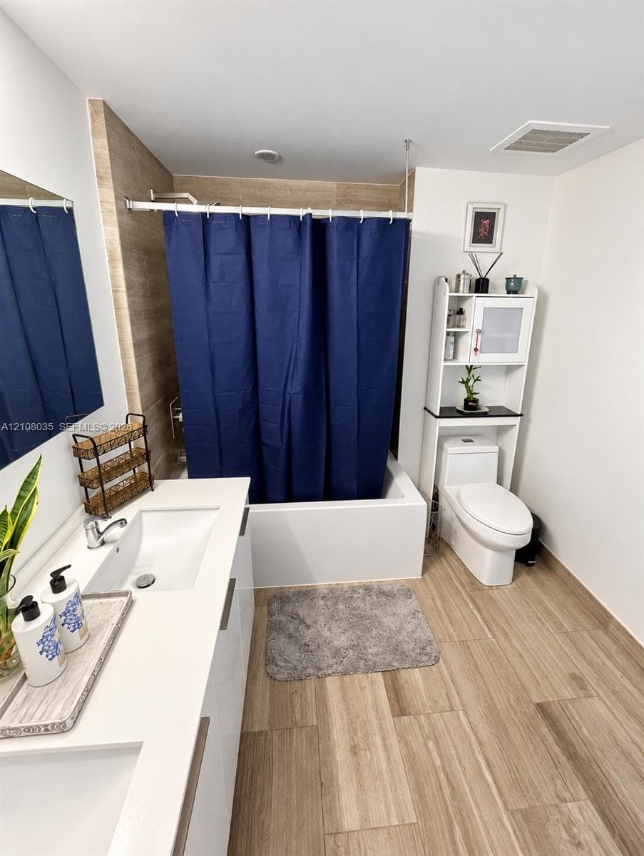 Modern bathroom featuring wood-finish tile flooring, a dual-sink vanity with a solid surface countertop, and a shower-tub combination with wall-to-wall tiling