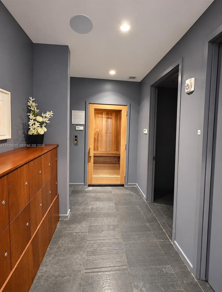 Hallway featuring integrated wood-finish lockers, dark stone-style tile flooring, and a dedicated sauna with a wood-framed glass door