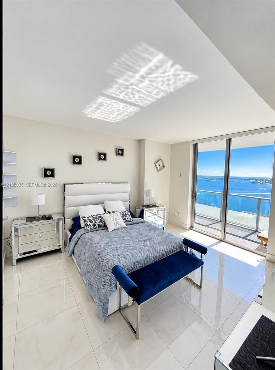 Floor-to-ceiling sliding glass doors opening to a glass-railed balcony, polished large-format tile flooring, and neutral wall finishes
