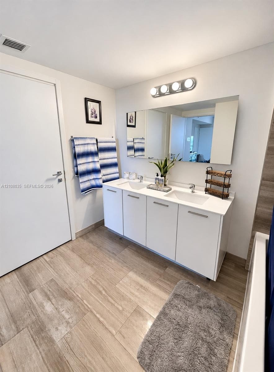 Double vanity featuring white cabinetry, a solid-surface countertop with integrated dual sinks, chrome-finish hardware, and a wall-mounted rectangular mirror with a four-light fixture