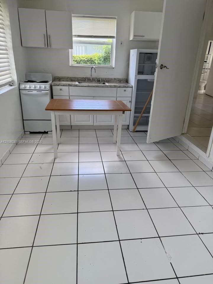 Kitchen featuring white cabinetry, stone-finish countertops, ceramic tile flooring, and a window over the stainless steel sink