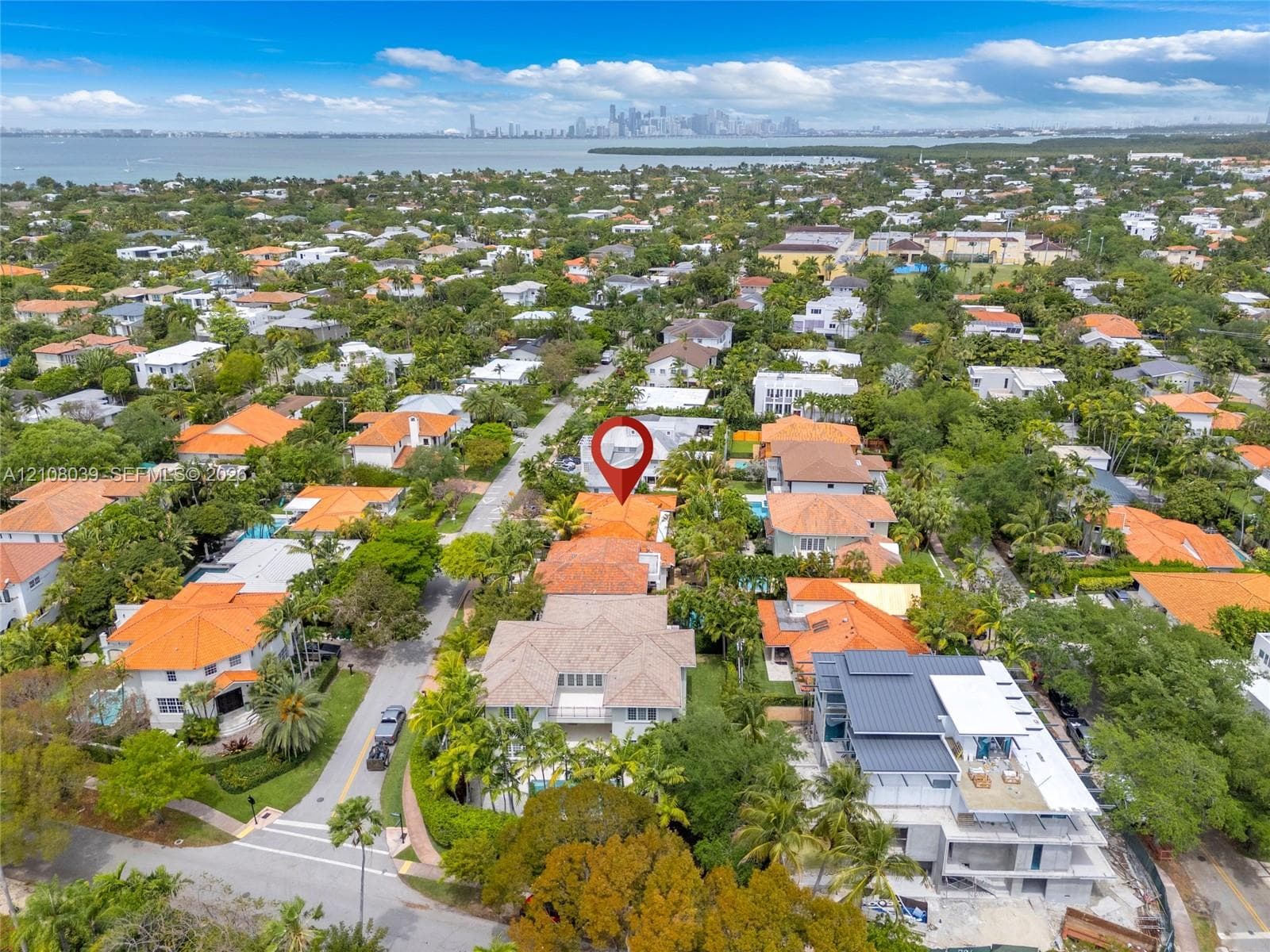 Aerial perspective of a residential property featuring a tiled roof, mature tropical landscaping, and a waterfront location with a distant urban skyline