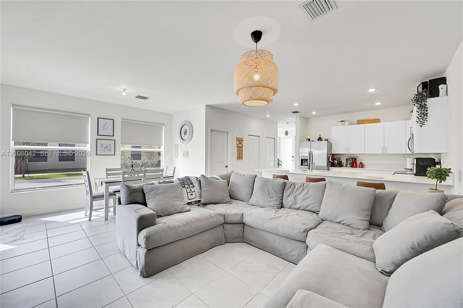 Open-concept interior featuring light-toned tile flooring, recessed lighting, a woven pendant light fixture, and white cabinetry