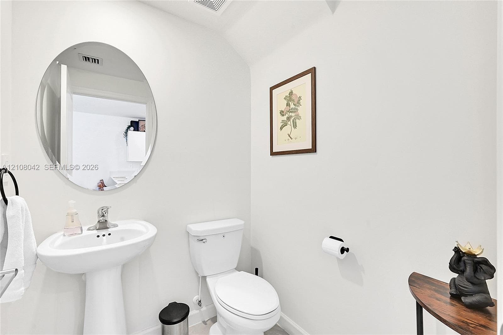 Pedestal sink with a polished chrome faucet, oval wall-mounted mirror, and standard-height toilet