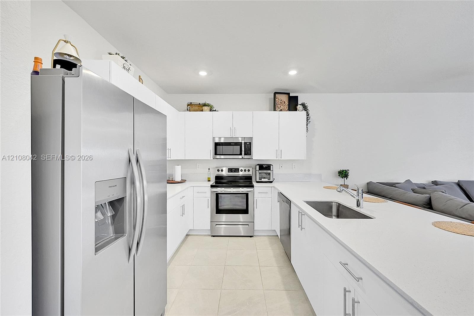 Kitchen featuring white cabinetry, solid-surface countertops, stainless steel appliances, a double-basin stainless steel sink, and tile flooring