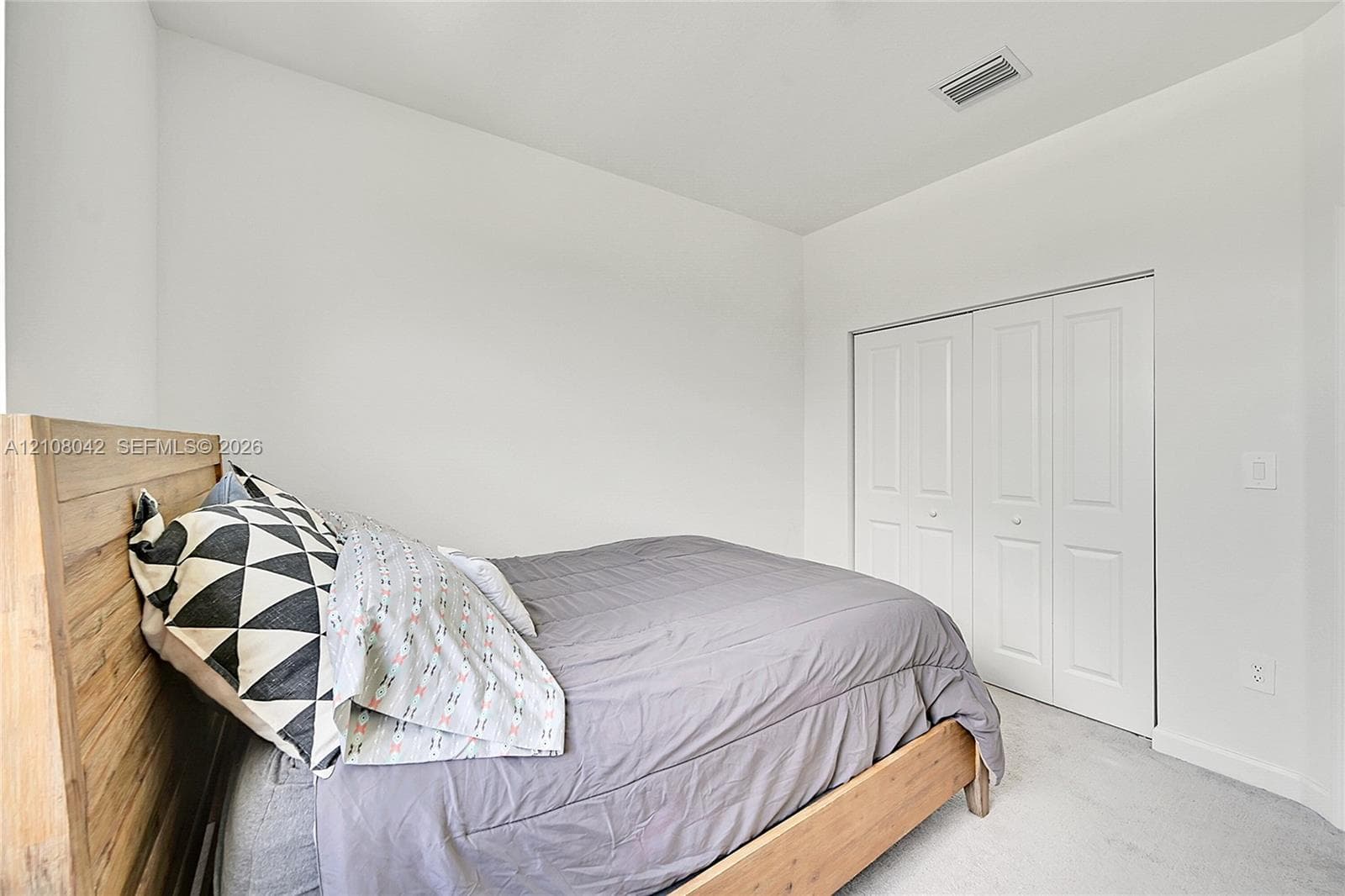 Neutral-toned interior space featuring light-colored carpeted flooring, white walls, and a white bi-fold closet door