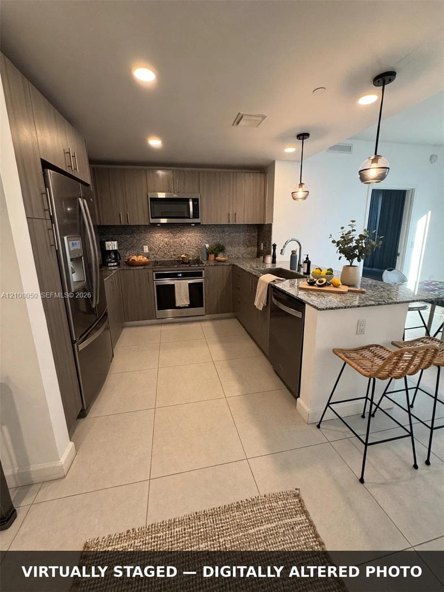 Kitchen featuring wood-finish cabinetry, stone countertops, stainless steel appliances, tile flooring, and dual pendant lighting