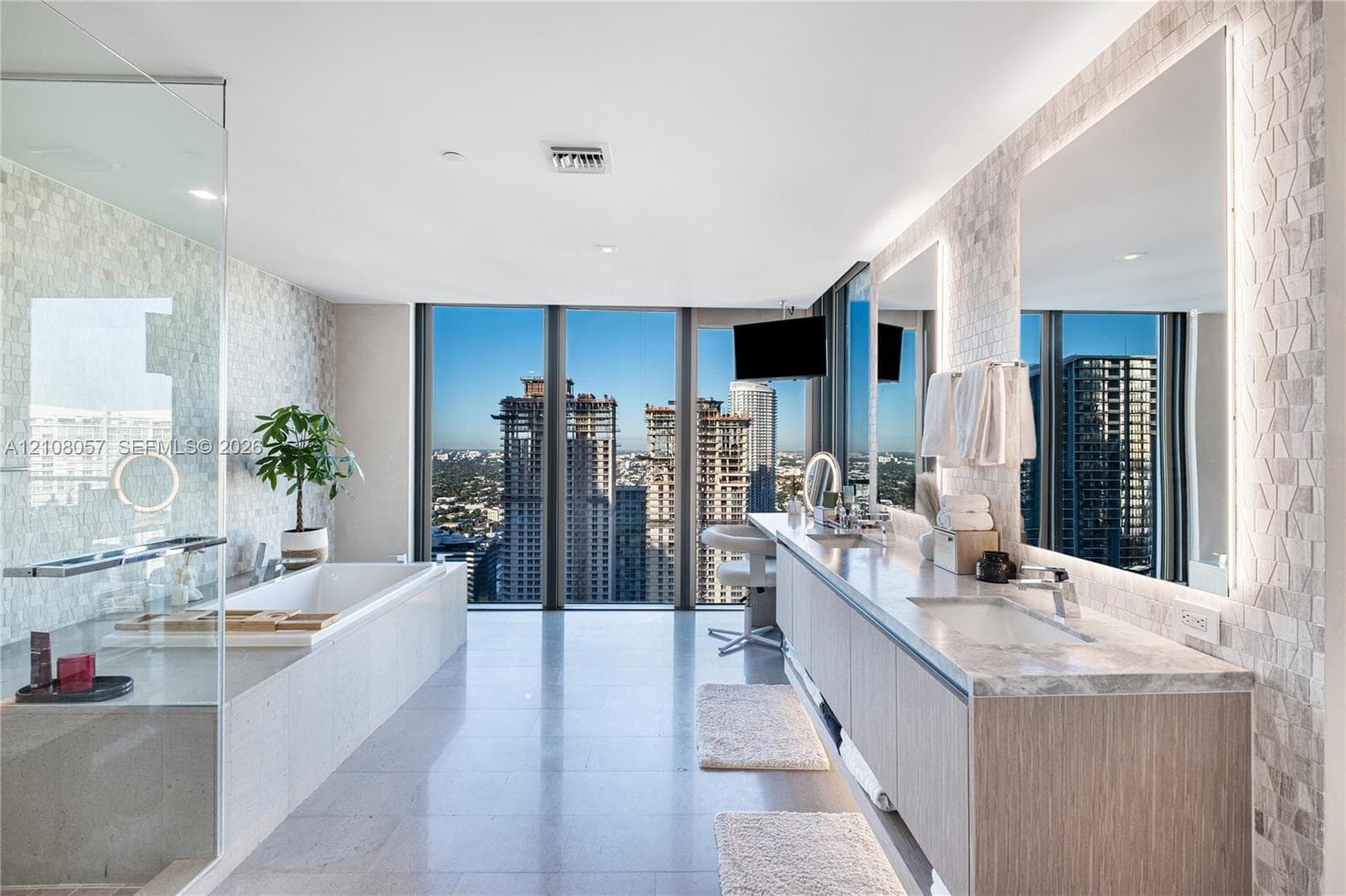 Floor-to-ceiling windows, dual-sink vanity with wood-finish cabinetry, stone countertop, glass-enclosed shower, and built-in soaking tub