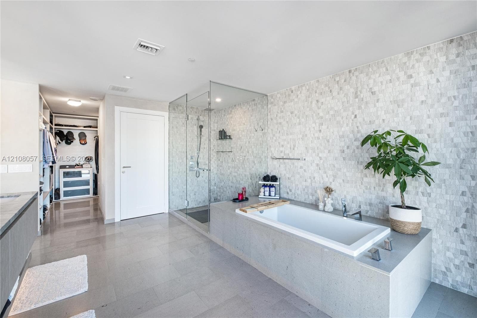 Bathroom featuring a deep-soaking drop-in tub with a stone-surround deck, a seamless glass-enclosed shower, stone mosaic wall tiling, large-format floor tile, and built-in closet shelving