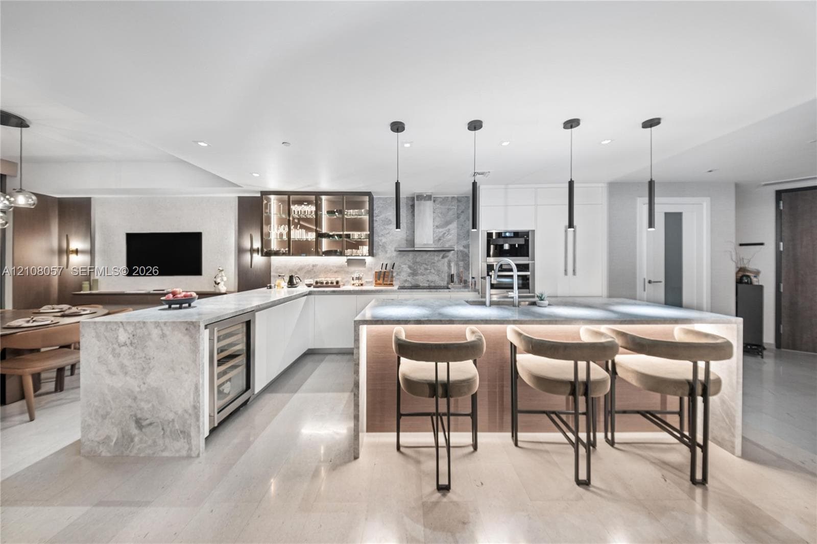 Gourmet kitchen featuring a waterfall-edge stone island, built-in wine refrigerator, under-cabinet lighting, floor-to-ceiling cabinetry, and modern pendant lighting