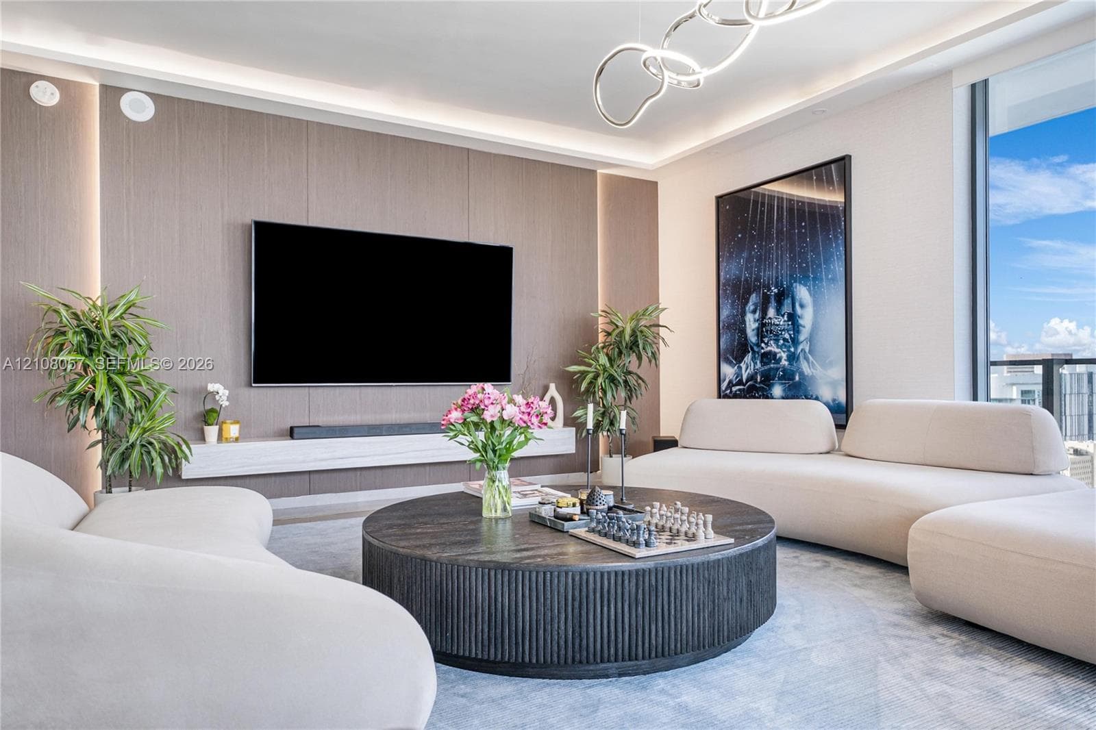 Living area featuring a floor-to-ceiling wood-panel accent wall, built-in floating media console, recessed perimeter lighting, and contemporary chandelier