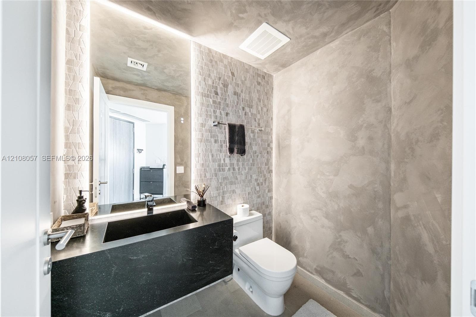Bathroom featuring textured wall finishes, a floating black countertop with an integrated basin, vertical recessed LED lighting, and mosaic-tiled accent wall