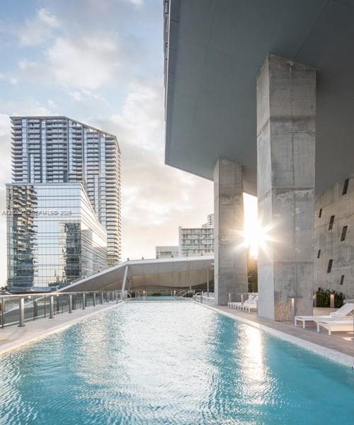 Outdoor swimming pool featuring a concrete deck, glass panel railings, and structural concrete columns