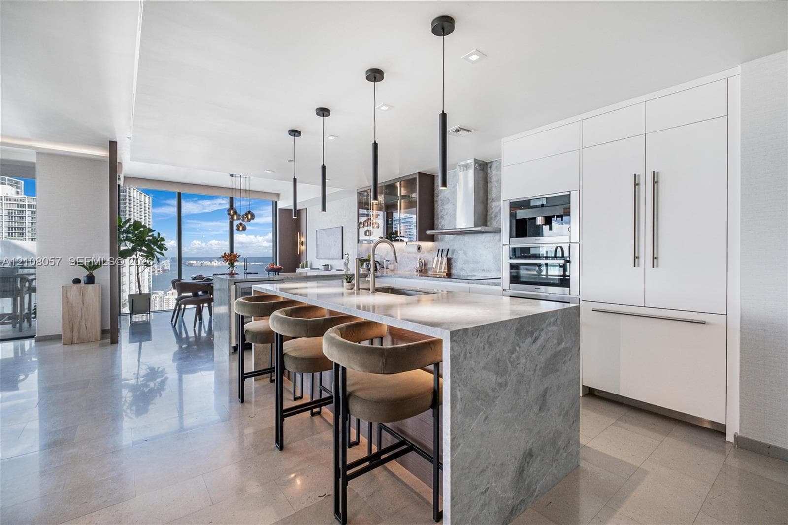 Kitchen featuring a stone-topped waterfall island, built-in stainless steel appliances, floor-to-ceiling cabinetry, stone flooring, and contemporary pendant lighting