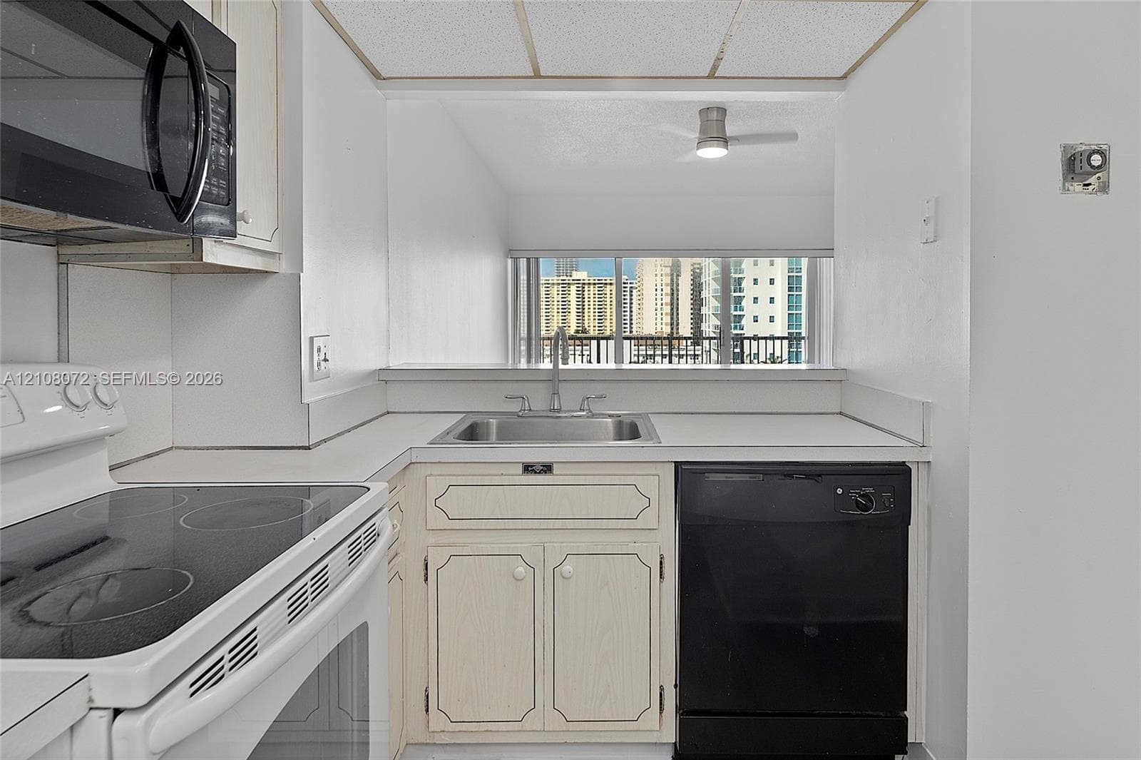 Kitchen featuring white cabinetry, integrated stainless steel sink with metal faucet, black dishwasher, and black over-the-range microwave