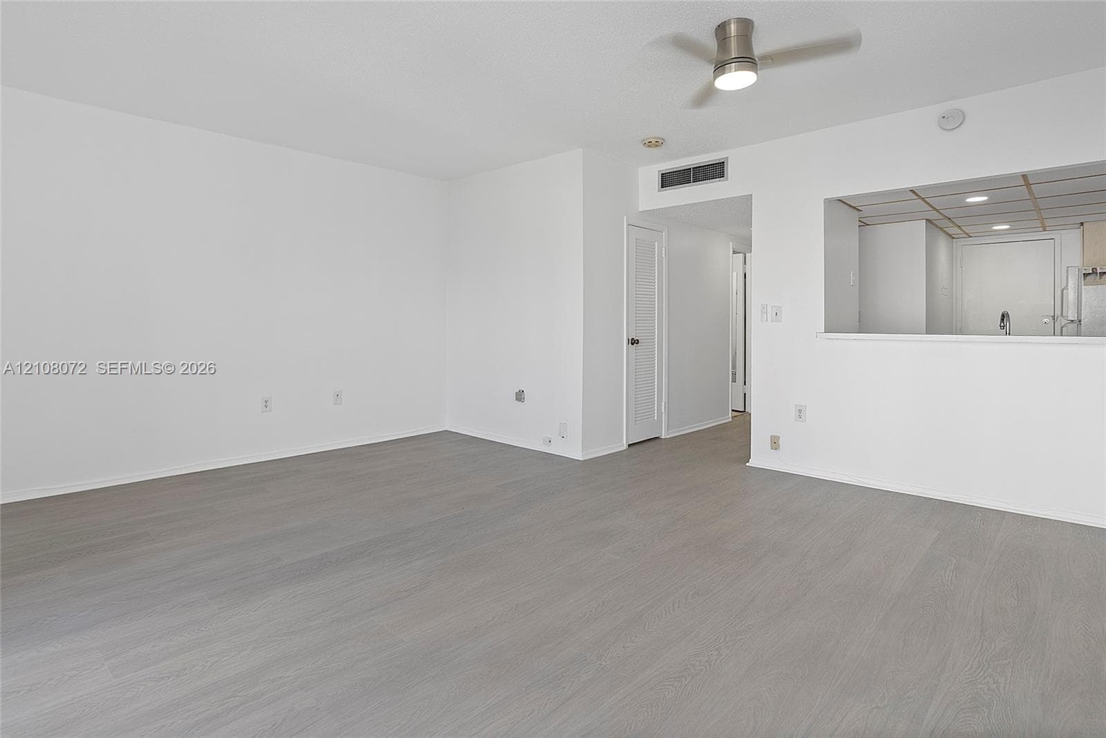 Open living area featuring wood-finish flooring, neutral wall paint, and a ceiling-mounted light fixture with fan