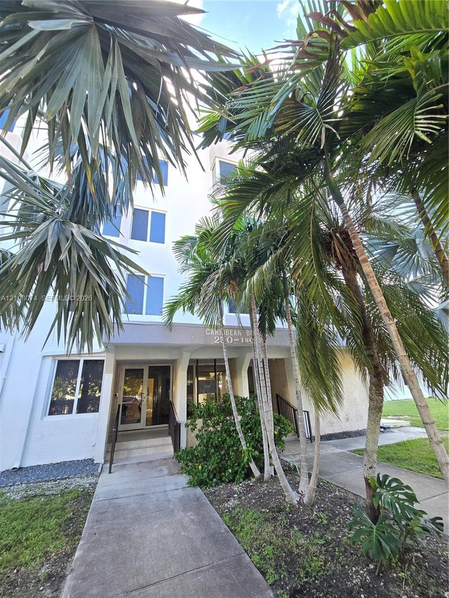 Multi-story exterior featuring light-toned facade, concrete walkway, and mature palm landscaping