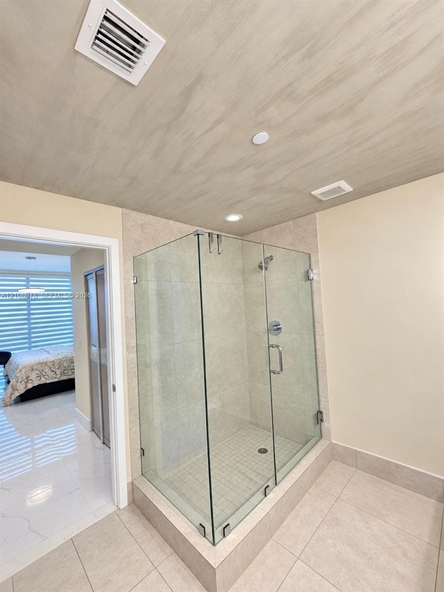 Frameless glass walk-in shower with neutral tile surround, metallic fixtures, and recessed lighting