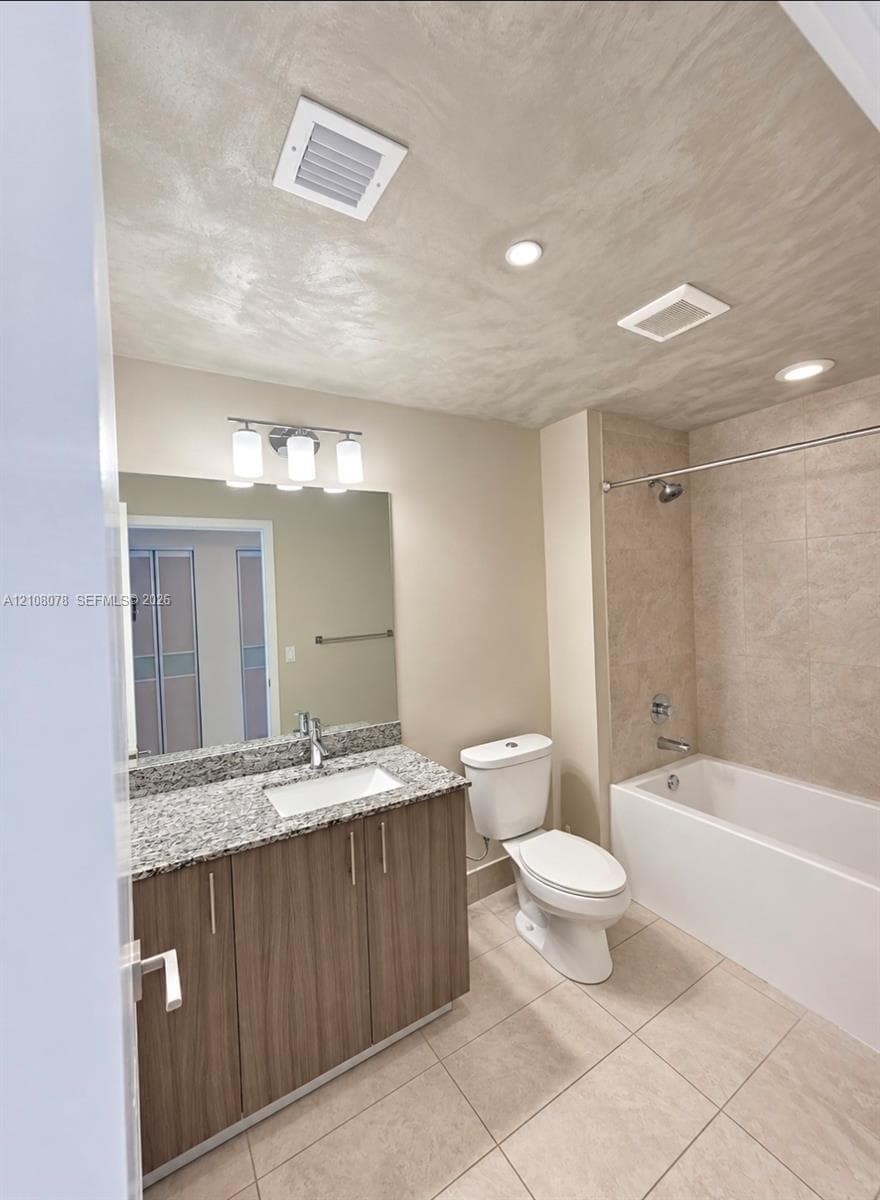Bathroom featuring a stone-look countertop, wood-finish cabinetry, a large wall-mounted mirror, recessed lighting, and a tiled shower-tub combination
