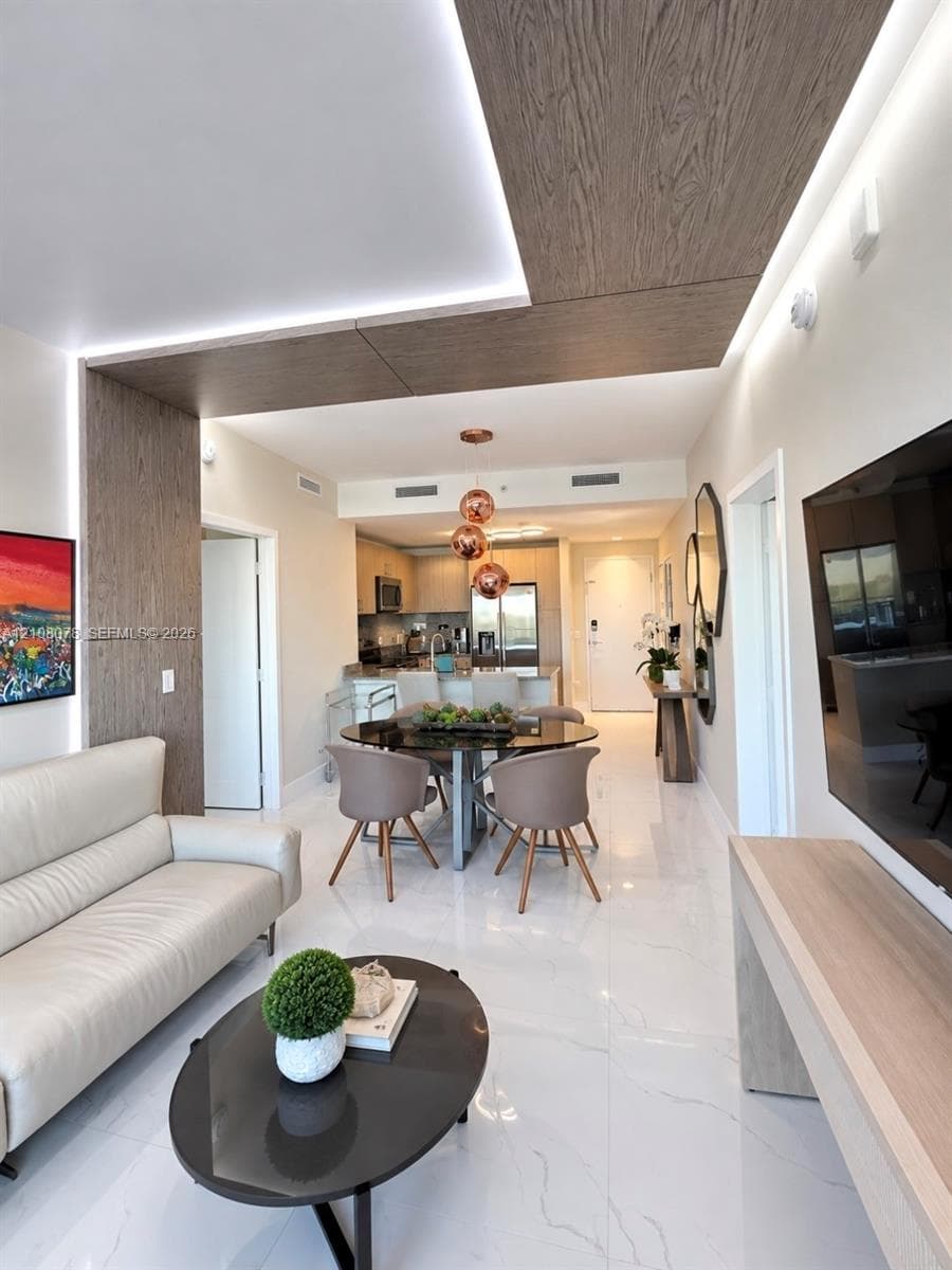 Open-concept living space featuring high-gloss tile flooring, integrated ceiling cove lighting, and wood-finish architectural paneling