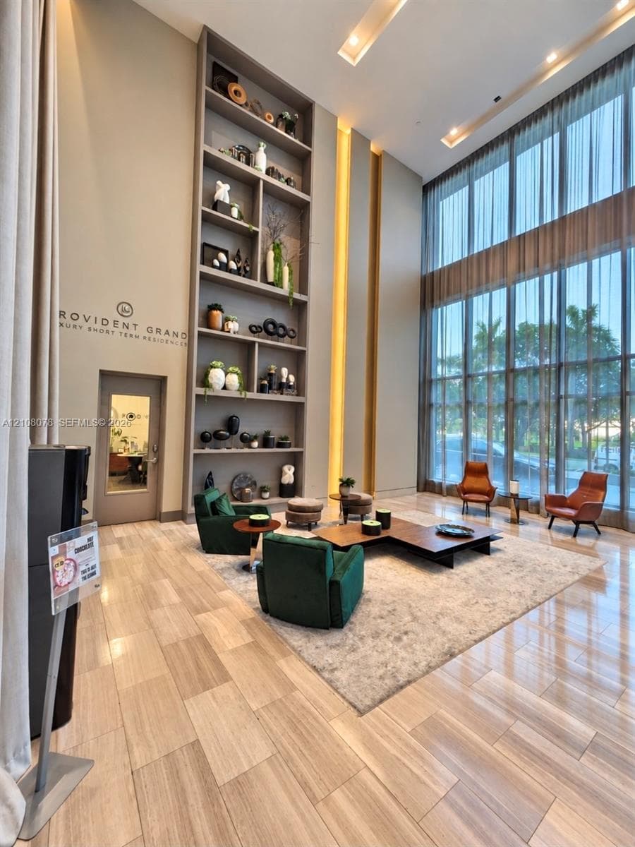 Double-height floor-to-ceiling windows, full-wall custom built-in shelving, recessed ceiling lighting, and polished large-format tile flooring