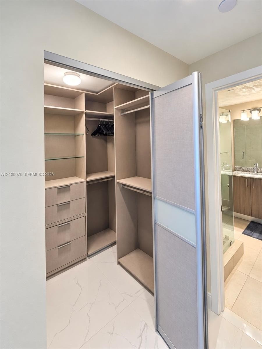 Walk-in closet featuring custom built-in cabinetry, integrated shelving, glass display surfaces, and a sliding door with frosted panel inserts