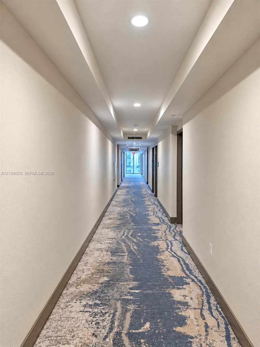 Hallway featuring neutral wall finishes, recessed ceiling lighting, tray ceiling detail, and patterned carpeting
