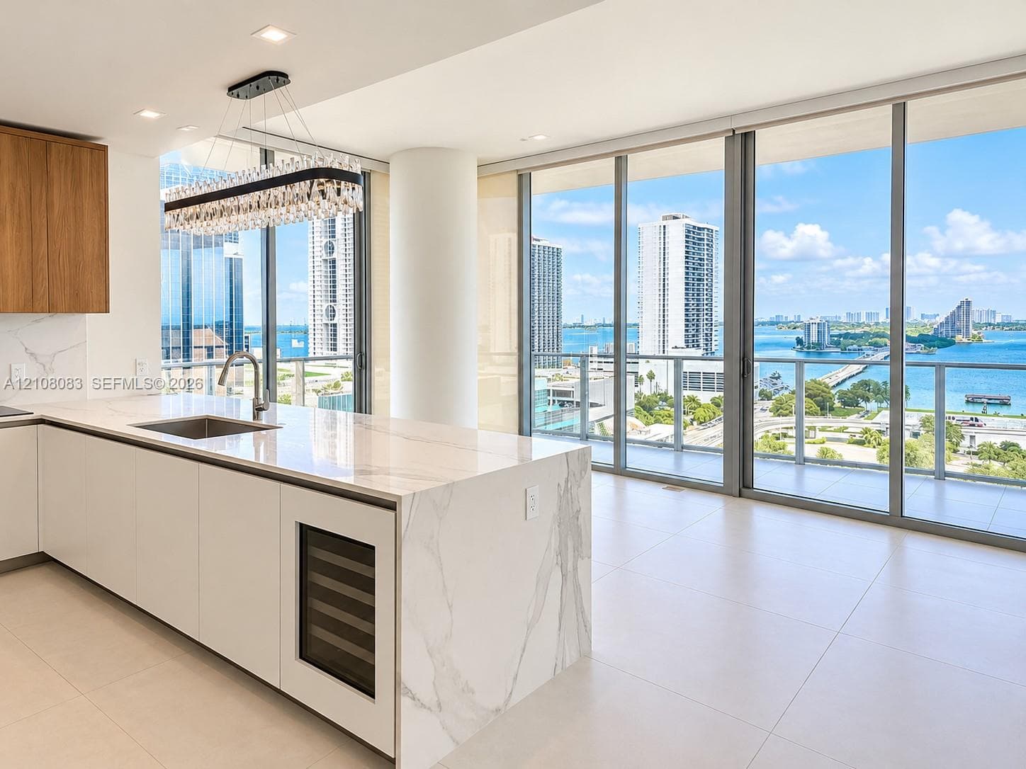 Kitchen featuring a large island with a waterfall-edge countertop, floor-to-ceiling glass panel walls, tile flooring, built-in wine cooler, and custom wood-finish cabinetry