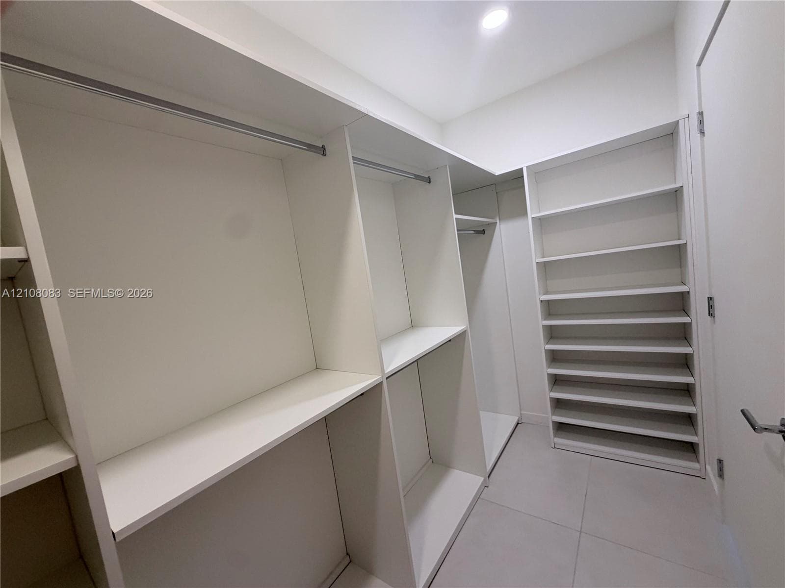 Walk-in closet featuring white built-in shelving, integrated hanging rods, and large-format tile flooring