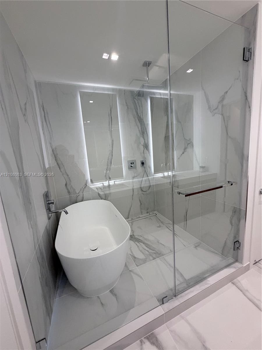 Wet room featuring floor-to-ceiling large-format stone-patterned tile, a freestanding oval soaking tub, and a frameless glass enclosure with a rainfall shower head