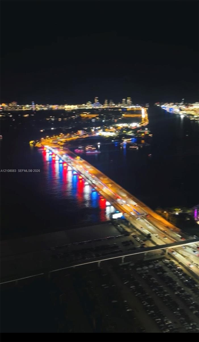 Aerial perspective featuring illuminated cityscape, expansive waterway, and bridge infrastructure