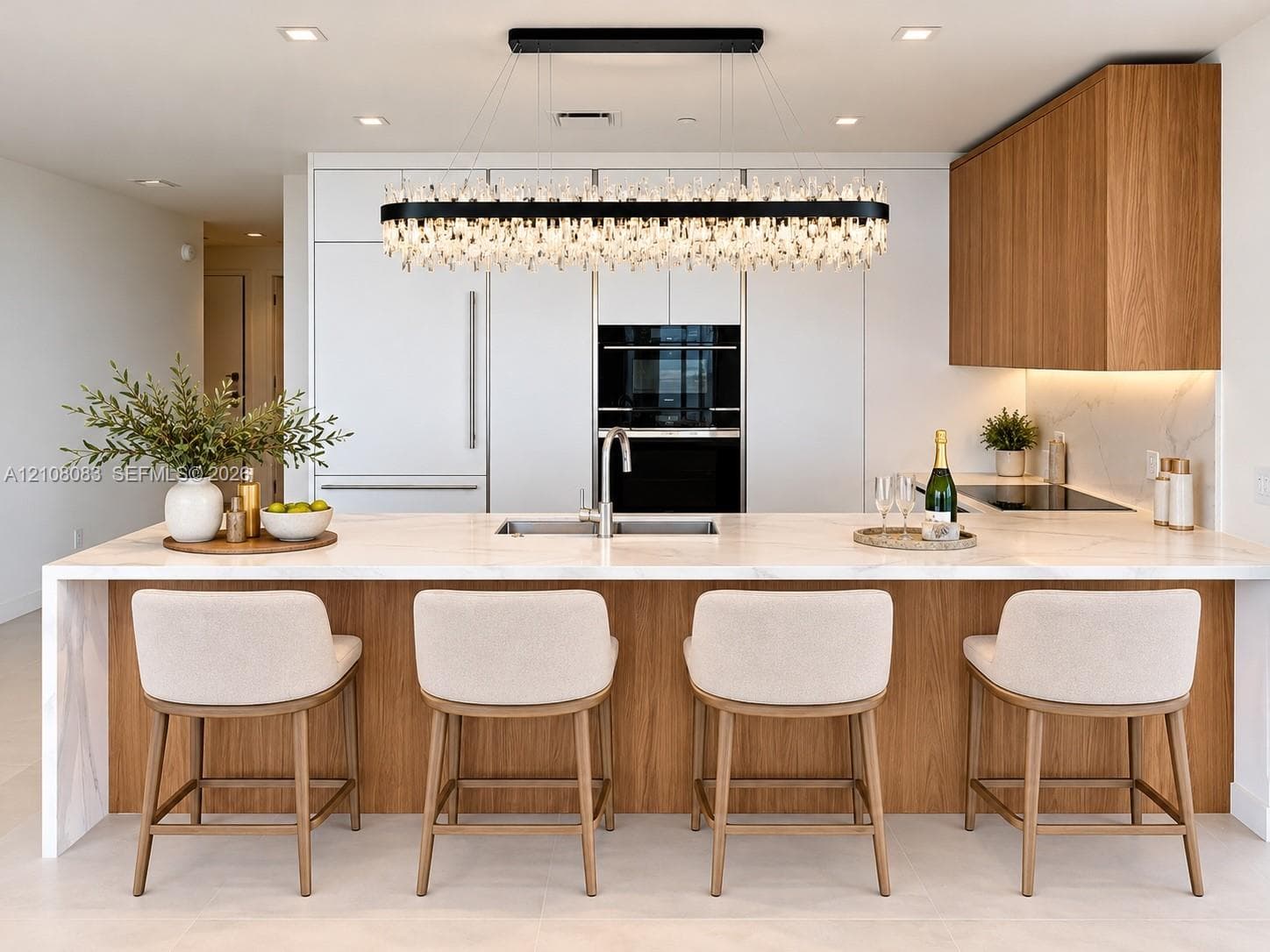 Kitchen featuring a waterfall-edge island with stone-surface countertop, flat-panel wood cabinetry, integrated appliances, and a linear crystal chandelier