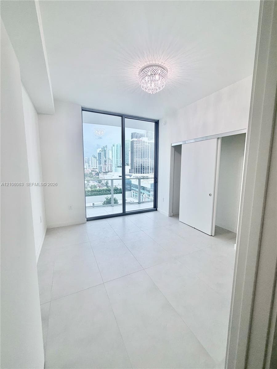 Floor-to-ceiling sliding glass doors, large-format tile flooring, crystal-accented flush mount lighting, and a sliding door closet