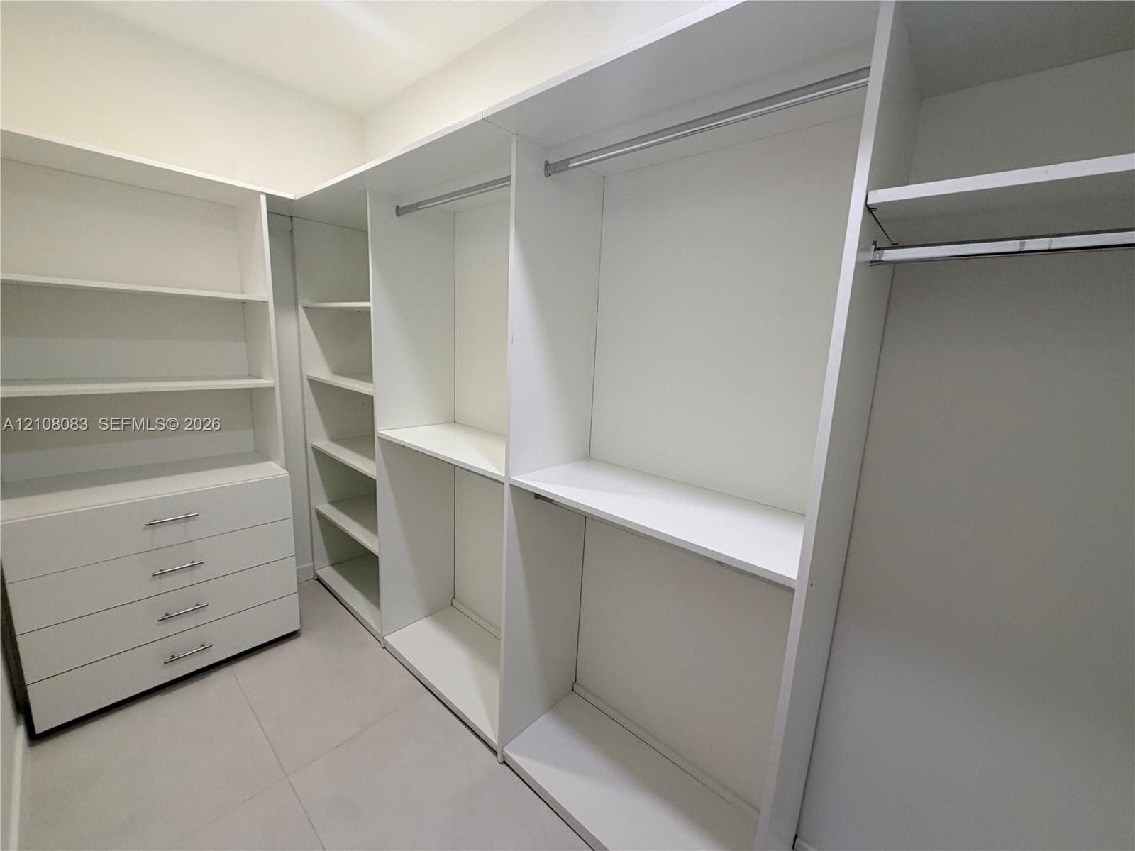Custom walk-in closet featuring white built-in shelving, multiple hanging rods, integrated four-drawer dresser, and tile flooring