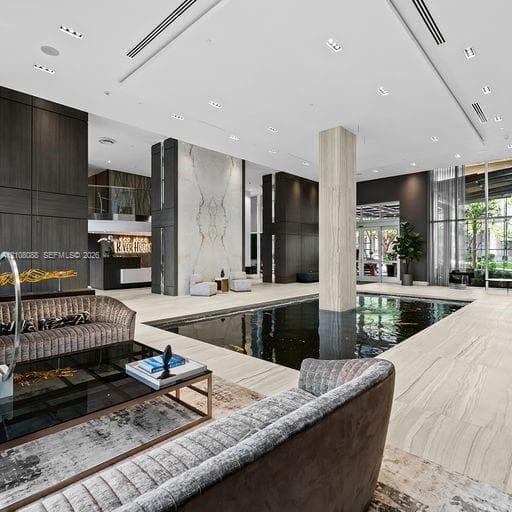 Lobby area featuring large-format tile flooring, a centered indoor water feature, stone-accented columns, floor-to-ceiling glass windows, and recessed ceiling lighting