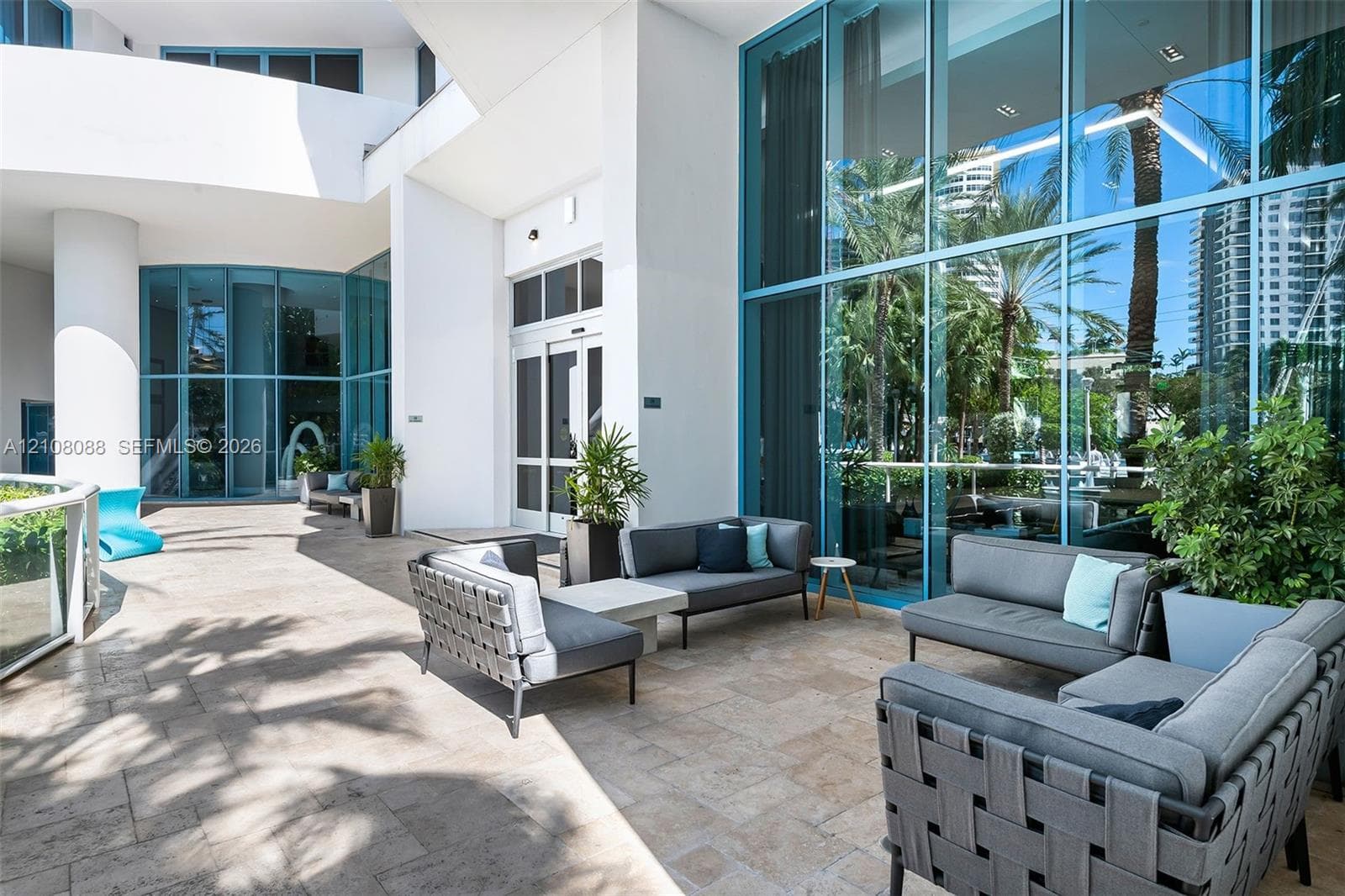 Covered terrace featuring stone tile flooring, floor-to-ceiling glass paneling, and prominent white architectural columns
