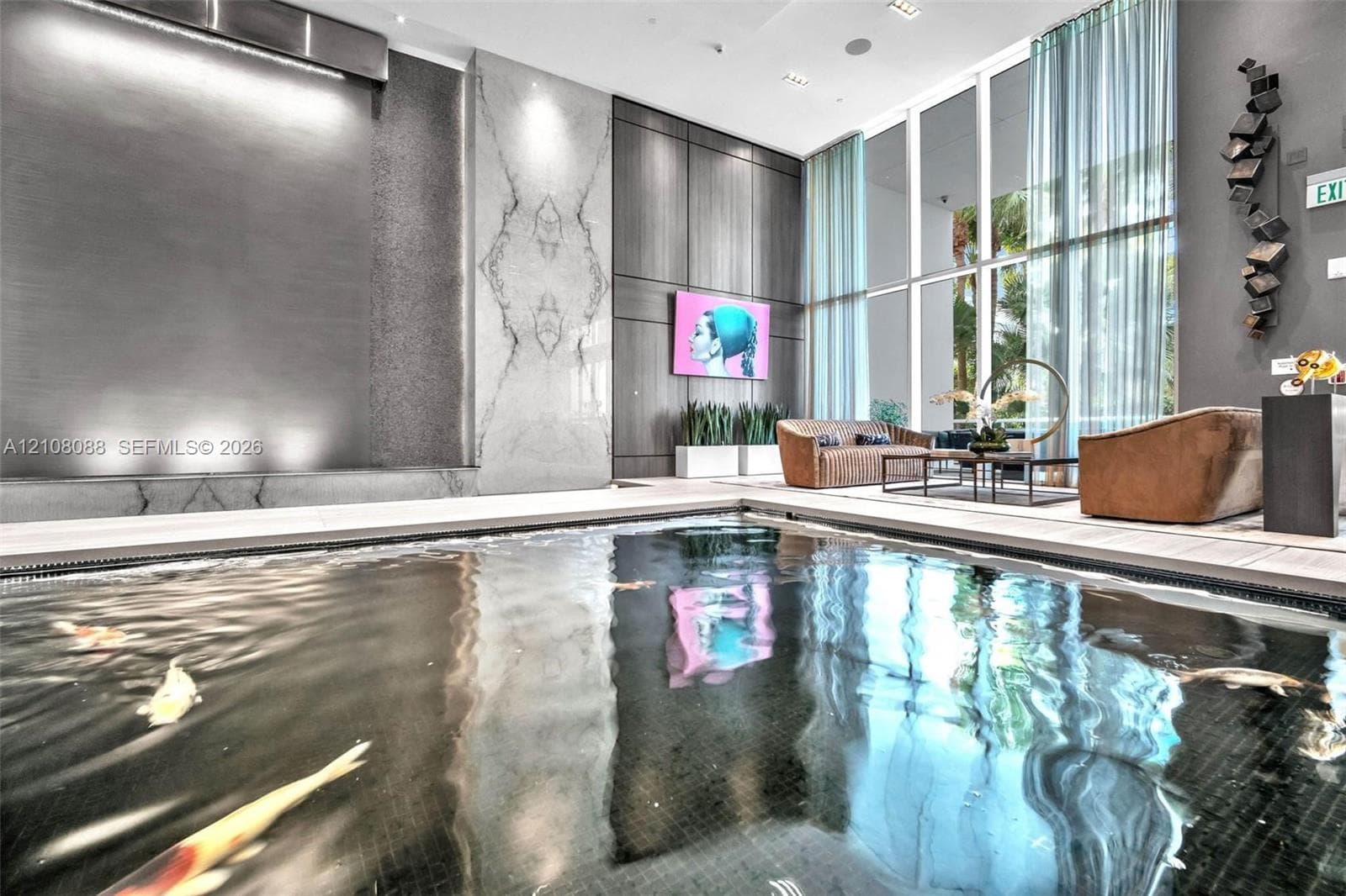 Indoor water feature with a dark-tiled basin, integrated wall-mounted waterfall, floor-to-ceiling windows, and decorative stone accent wall
