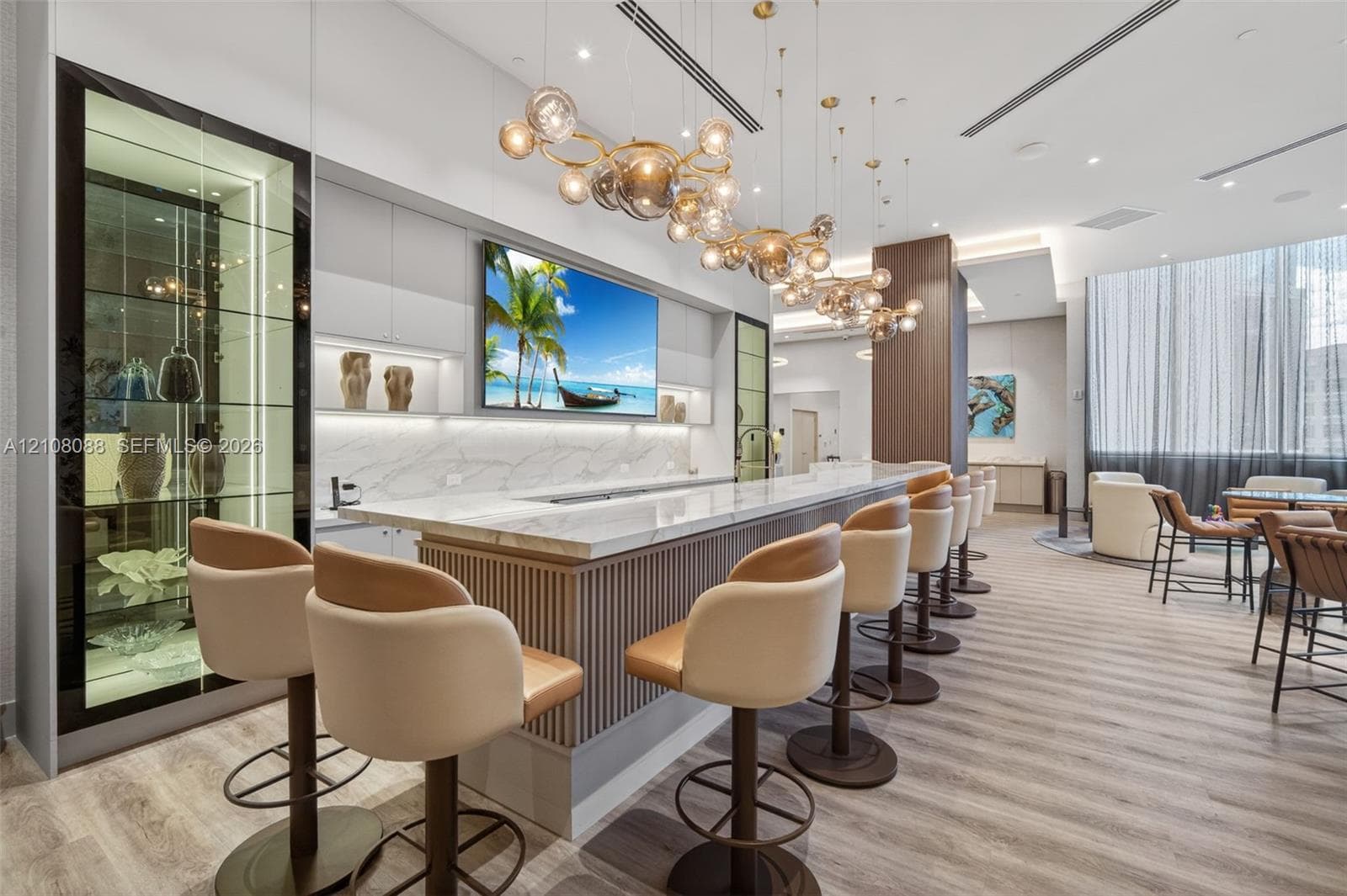 Custom bar area featuring a light-toned countertop, a fluted-panel base, integrated glass-front display cabinetry, and multi-globe pendant lighting, all set above wood-finish flooring
