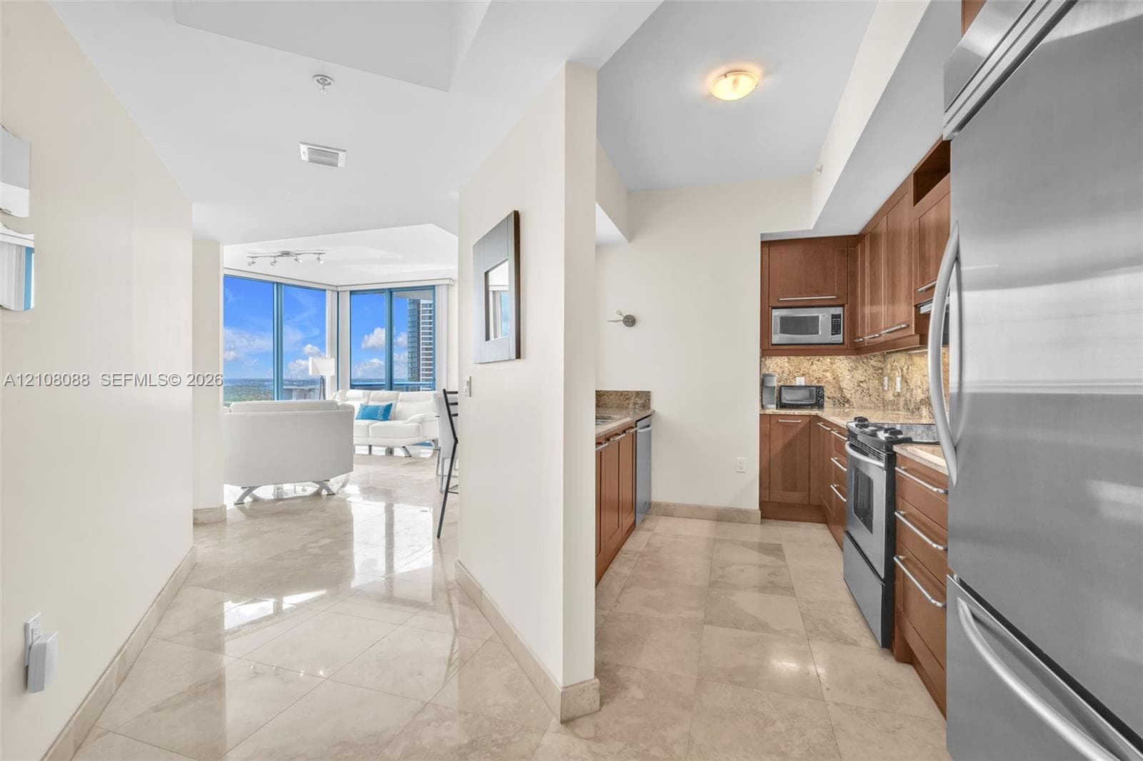 Entry and kitchen featuring wood cabinetry, stone countertops, stone flooring, and stainless steel appliances, with floor-to-ceiling windows