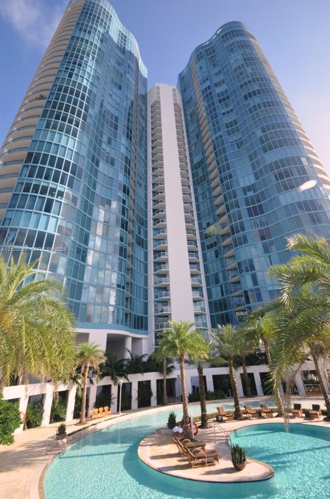 High-rise glass facade featuring curvilinear architecture, private balconies, and a multi-level swimming pool with hardscaped patio