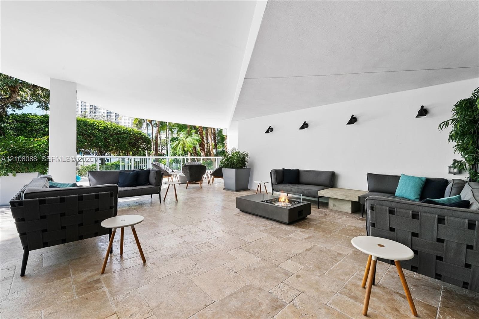 Covered outdoor terrace featuring natural stone flooring, a built-in fire feature, wall-mounted sconce lighting, and a white metal perimeter railing