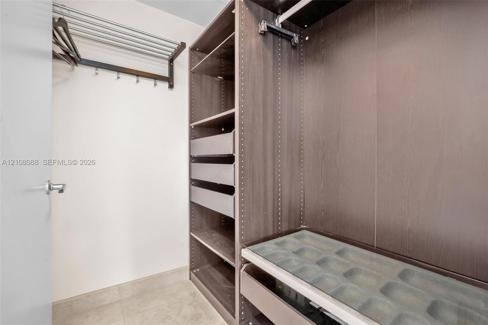 Walk-in closet featuring custom wood-finish cabinetry, built-in shelving, integrated pull-out drawers, a glass-topped accessory organizer, and wall-mounted garment racks